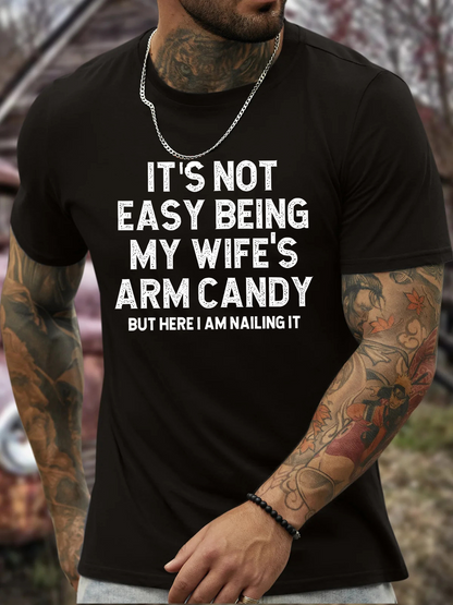 Men's Graphic T-Shirt Its Not Easy Being My Wifes Arm Candy Here I Am Nailing It Bold White Lettering On Solid Black Cotton Shirt